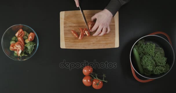 Homem cortando tomate na tábua de corte de madeira perto de outros vegetais. Vista superior . — Vídeo de Stock