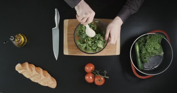 O homem está misturando legumes na tigela. O homem está a malhar uma salada. estilo de vida saudável. Vista superior . — Vídeo de Stock