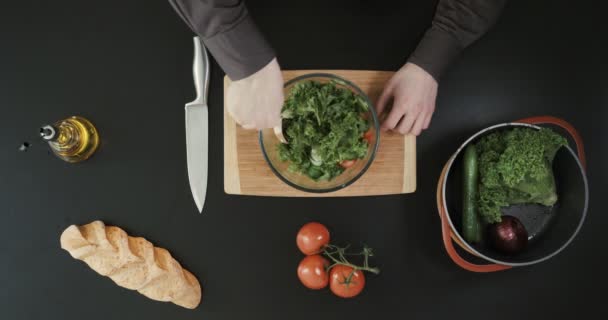 O homem está fazendo uma salada em uma tigela transparente bif. Outros legumes e pão colocados nas proximidades . — Vídeo de Stock