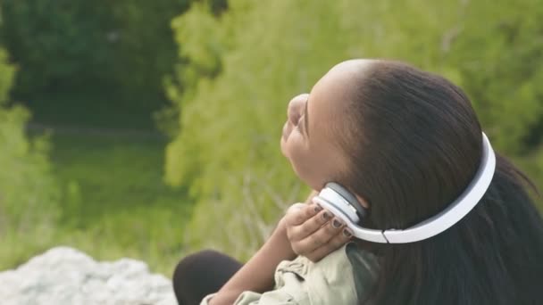 Szép afro-amerikai lány hallgatta a zenét a háttérben zöld park részlete. Szemközti nézet — Stock videók