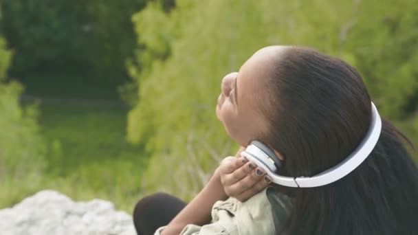 Primer plano de la encantadora chica afroamericana escuchando la música en el fondo del parque verde. Vista superior — Vídeo de stock