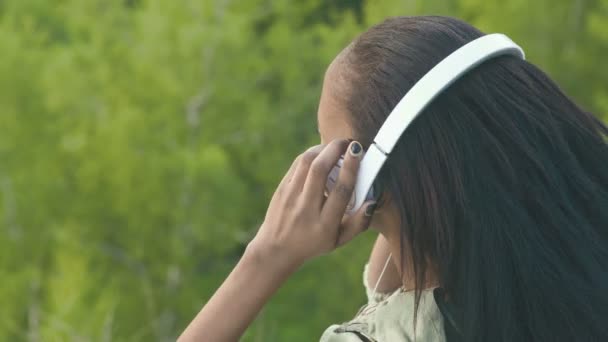 Primer plano de la encantadora chica afroamericana escuchando la música en el fondo del parque verde. Vista superior — Vídeos de Stock