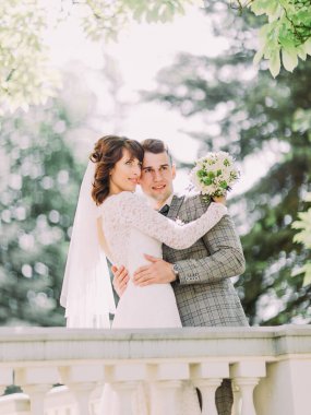 Gülümseyen yeni evliler varil yakın dururken sarılıyorlar. Yan görünüm.