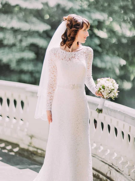 La foto lateral de la novia sosteniendo el ramo de bodas mientras está de pie en el balcón . — Foto de Stock