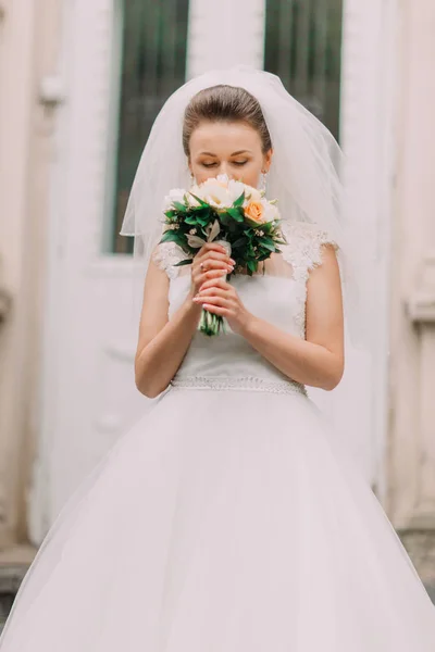 A noiva bonita está cheirando as flores do casamento enquanto está de pé nas escadas . — Fotografia de Stock