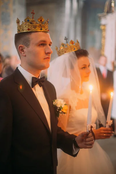 頭に金の冠と新婚夫婦は教会で結婚式中にキャンドルを保持しています。. — ストック写真
