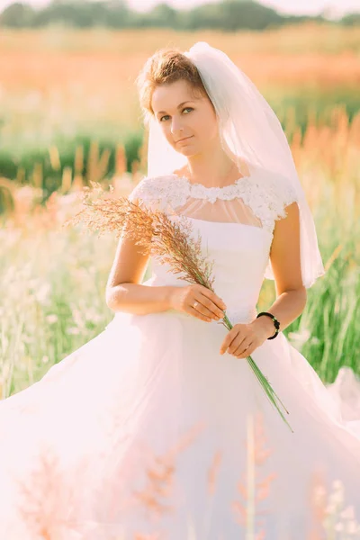O retrato vertical da noiva elegante segurando o wheatear no campo ensolarado . — Fotografia de Stock