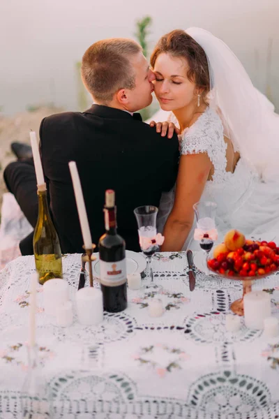 Der Bräutigam küsst die Braut auf die Wange hinter dem Picknickset. — Stockfoto