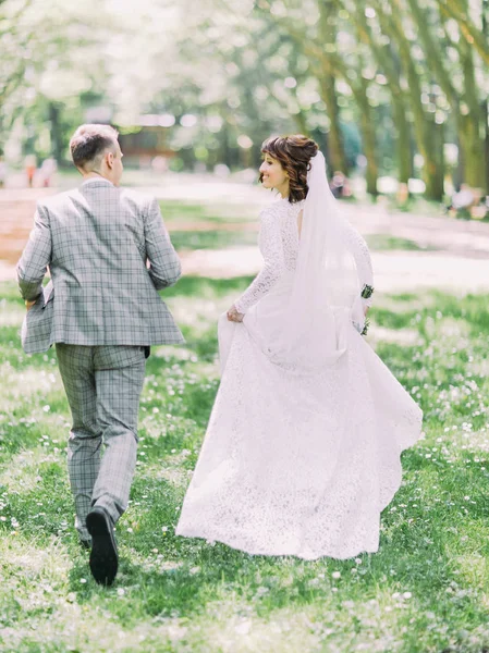 A visão traseira do casal recém-casado feliz correndo ao longo do parque ensolarado . — Fotografia de Stock