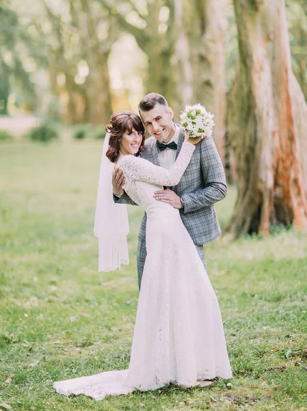 Le joli portrait complet des jeunes mariés souriants serrant dans leurs bras dans le parc . — Photo