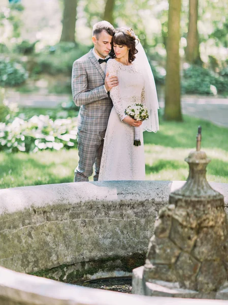 Le portrait sensible sur toute la longueur du marié enlacant la mariée derrière la fontaine . — Photo