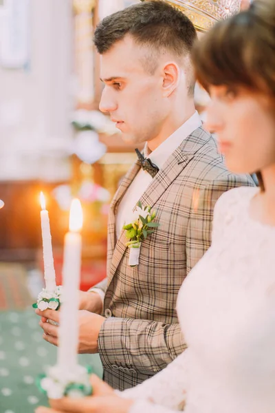 El retrato lateral del novio sosteniendo la vela en la iglesia . — Foto de Stock