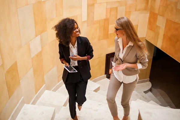 Toma de dos empresarias sonrientes subiendo. Mujeres con trajes. Una mujer es negra. . — Foto de Stock