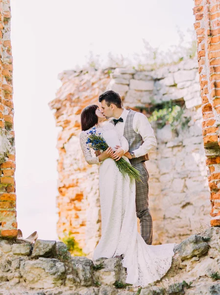 Volledige weergave van de kussen pasgetrouwden terwijl staande op de ruïnes van het gebouw. — Stockfoto
