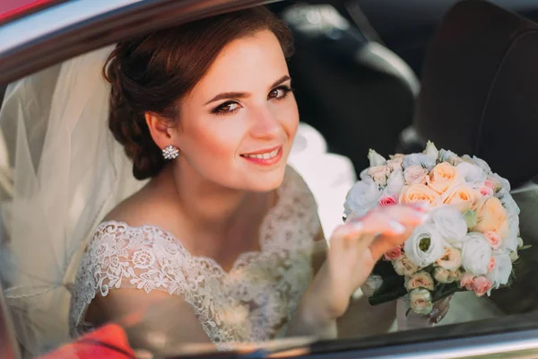 Retrato de cerca de la novia sonriente con el colorido ramo sentado en el coche . — Foto de Stock