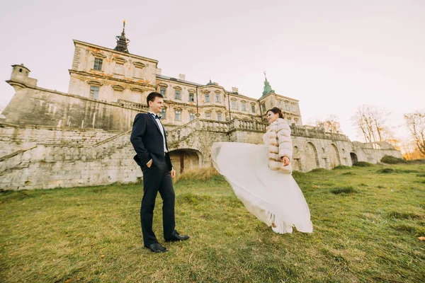 A szél az overblowing az esküvői ruha a menyasszony az antik gótikus palota közelében séta közben. — Stock Fotó