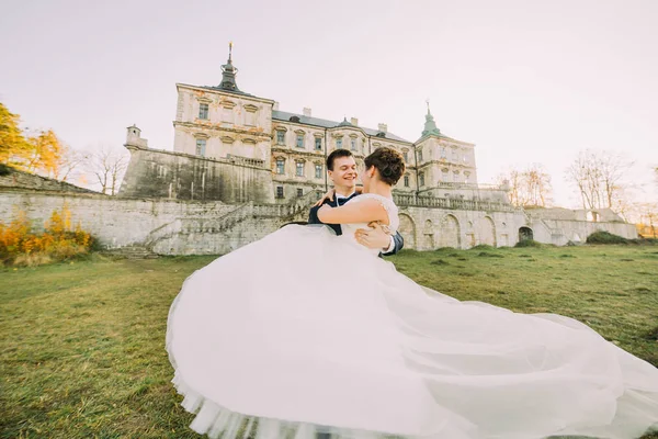 Feliz tempo a passar no castelo gótico. O noivo está carregando a noiva. A visão traseira da noiva . — Fotografia de Stock