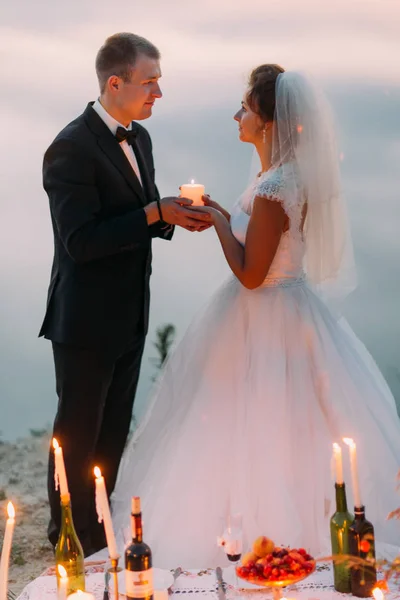 El romántico retrato lateral de la pareja recién casada sosteniendo la vela brillante detrás del juego de picnic . —  Fotos de Stock