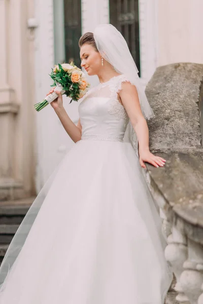 O retrato lateral sensível da noiva no vestido longo cheirando o buquê de flores amarelas . — Fotografia de Stock