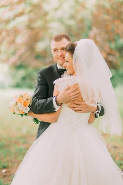 Die Rückenansicht der Braut mit nackten Schultern, die sich mit dem Bräutigam im herbstlichen Park umarmt. — Stockfoto