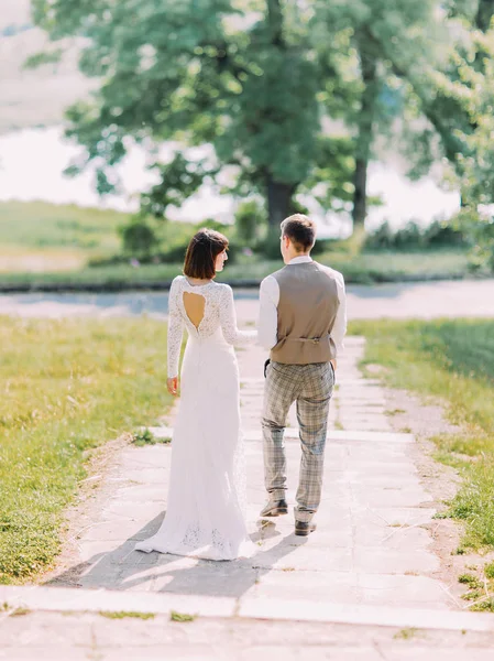 La vue arrière des jeunes mariés marchant le long du parc . — Photo