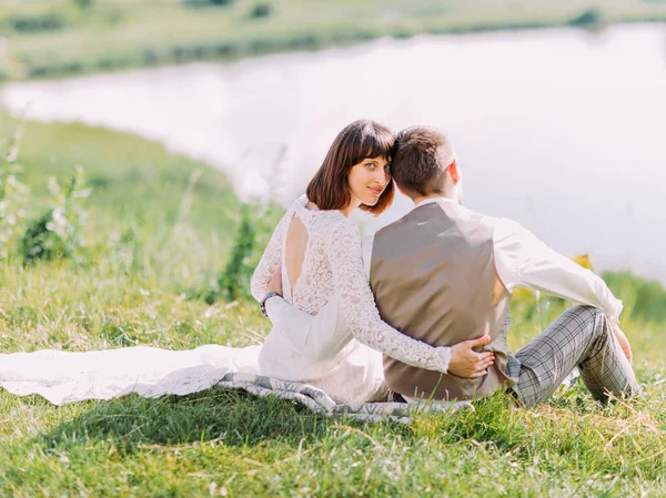 A visão traseira dos recém-casados sentados na grama e desfrutando da natureza . — Fotografia de Stock