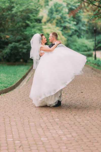 Foto sensible del novio feliz llevando a la novia sonriente en el parque . — Foto de Stock