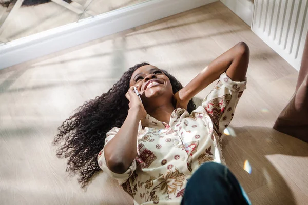 Happy černá žena ležící na podlaze a mluvil po telefonu. Žena s dlouhými tmavými vlasy. — Stock fotografie