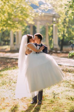 Damat gelini tutarak ve güneşli parkta öpüşme.