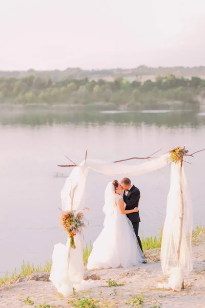De kussen jonggehuwde paar in de buurt van het prachtige uitzicht op de rivier. — Stockfoto