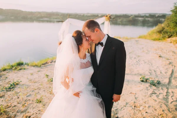 The horizontal close-up portrait of the smiling newlywed couple standing head-to-head at the background of the river. — Stock Photo, Image