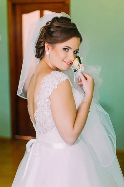 Jovem noiva inocente em vestido branco posando, segurando pequeno boutenniere bonito e olhando por cima de seu ombro — Fotografia de Stock