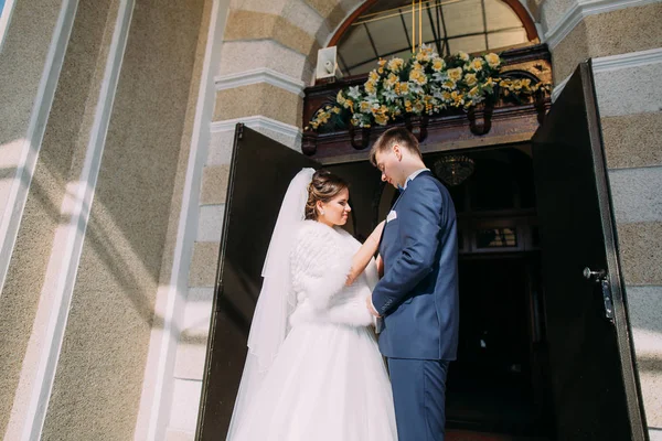 La vista horizontal de los recién casados felices de pie cerca de la iglesia . —  Fotos de Stock