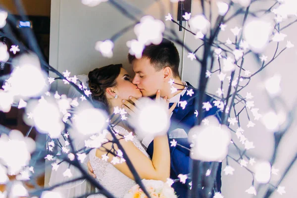 A visão de close-up dos recém-casados beijando por trás das guirlandas luz wight . — Fotografia de Stock