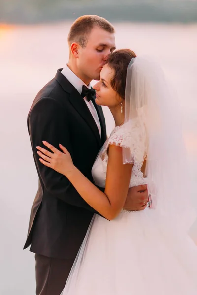 Le portrait en gros plan sensible du marié embrassant la mariée sur le front . — Photo