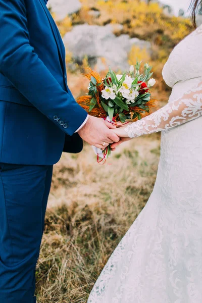 Vista da vicino delle mani degli sposi che tengono il bouquet nuziale delle rose colorate . — Foto Stock