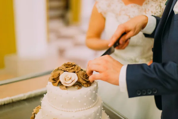 As mãos do noivo cortando a primeira parte do bolo de casamento . — Fotografia de Stock