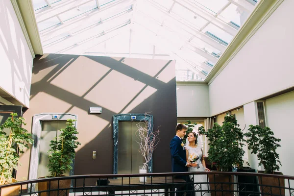 Braut und Bräutigam schauen sich an. Hotellobby dekoriert mit verschiedenen exotischen Pflanzen als Hintergrund — Stockfoto