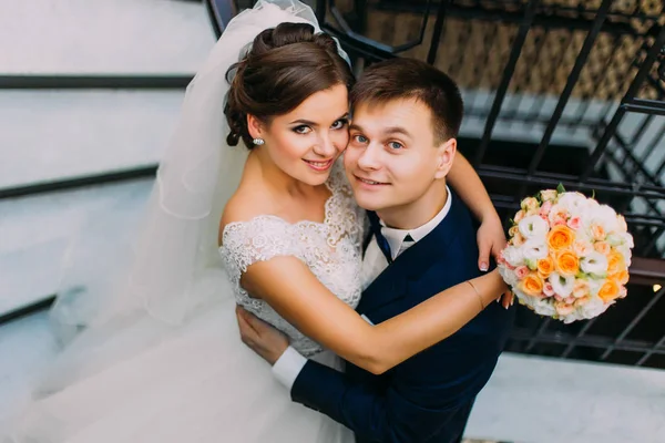 Câlin joyeux jeunes mariés debout près des escaliers. Le portrait ci-dessus . — Photo