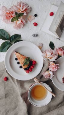 Kahvaltı lezzetli bileşimi. Pembe güller ve otlar ile meyve pasta fincan çay ve masaya güzel yerleştirilen kitap ile dekore edilmiş.