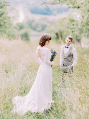 Gelin ile damadın alanında arka plan bulanık mavi çiçeklere arkadan görünüm.