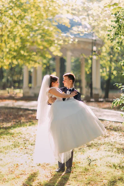 Le marié tient la mariée dans la longue robe blanche dans le parc . — Photo