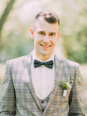 Parkta gülümseyen damat dikey portresi.