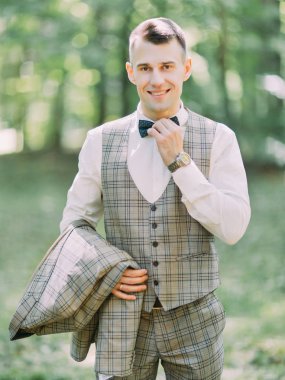 Onun papyon parkta dokunmadan yakışıklı gülümseyen damat dikey görünüm.