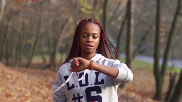 La chica afroamericana está mirando a la mano mientras trota en el parque . — Vídeo de stock