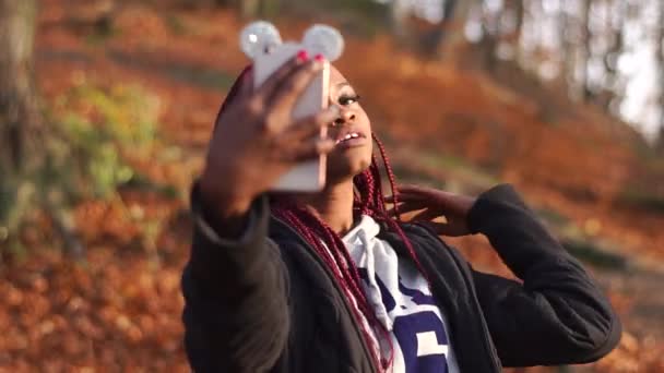 Afro-american dívka se dotýká vlasy a s selfie v podzimní park. — Stock video