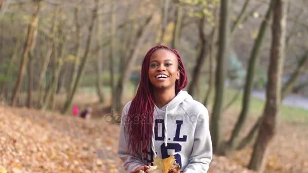 Gelukkig Afro-Amerikaanse meisje is leuk in de herfst park scheren. Ze is het gooien van de vergeelde bladeren. — Stockvideo