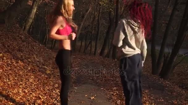 Ganzkörperansicht der blonden und afroamerikanischen Mädchen, die kopfschüttelnd im herbstlichen Park springen. — Stockvideo