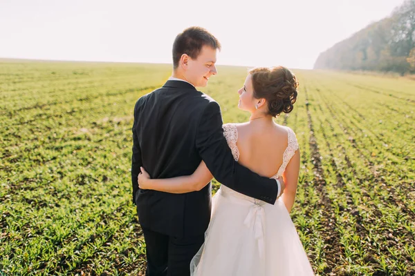 Der Rücken der umarmten und lächelnden Frischvermählten, die ihre Zeit auf dem Feld verbringen. — Stockfoto