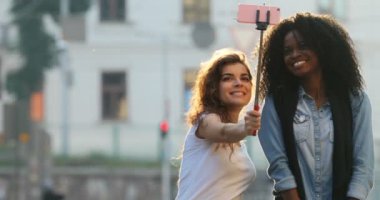 Neşeli kız komik surat ve cadde boyunca yürürken selfie stick kullanarak fotoğraf çekmek.